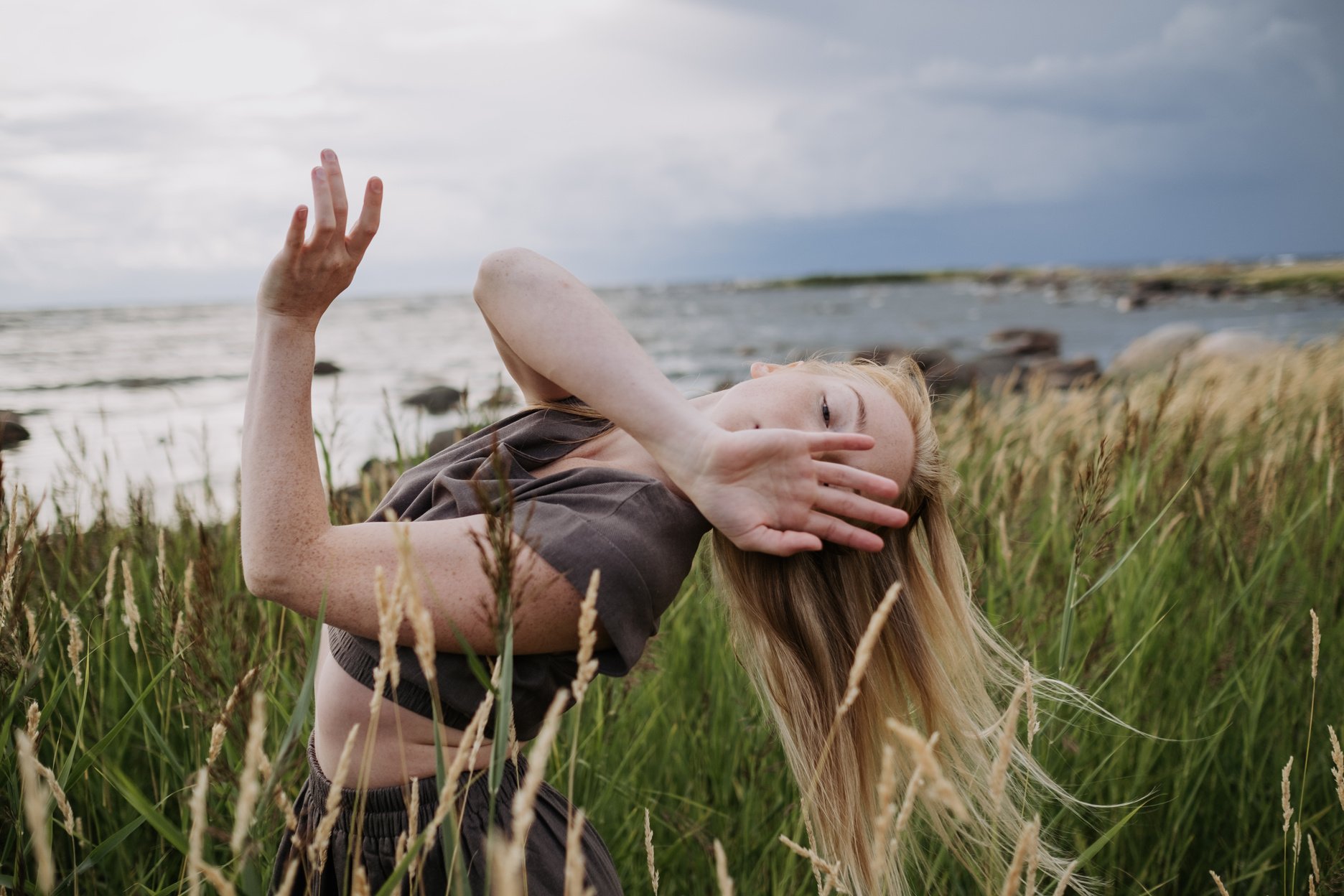 A Woman in Gray Shirt Dancing on Green Grass Field