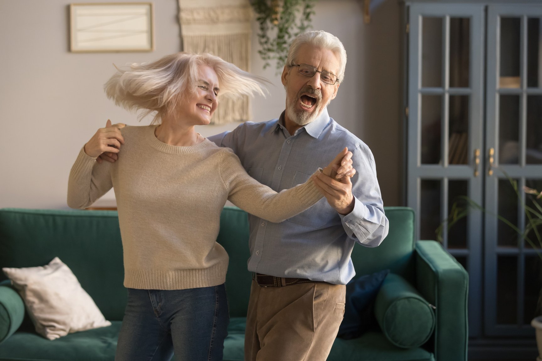 Carefree happy active old couple dancing laughing in living room