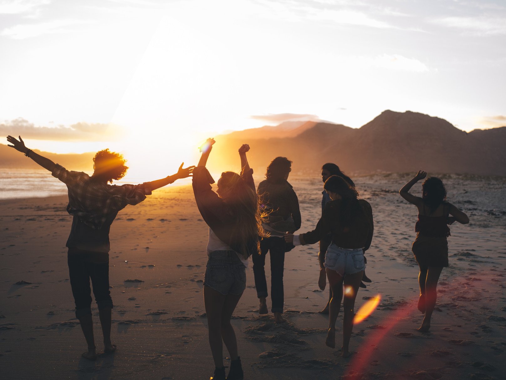 Teen friends dancing on the beach at sunset